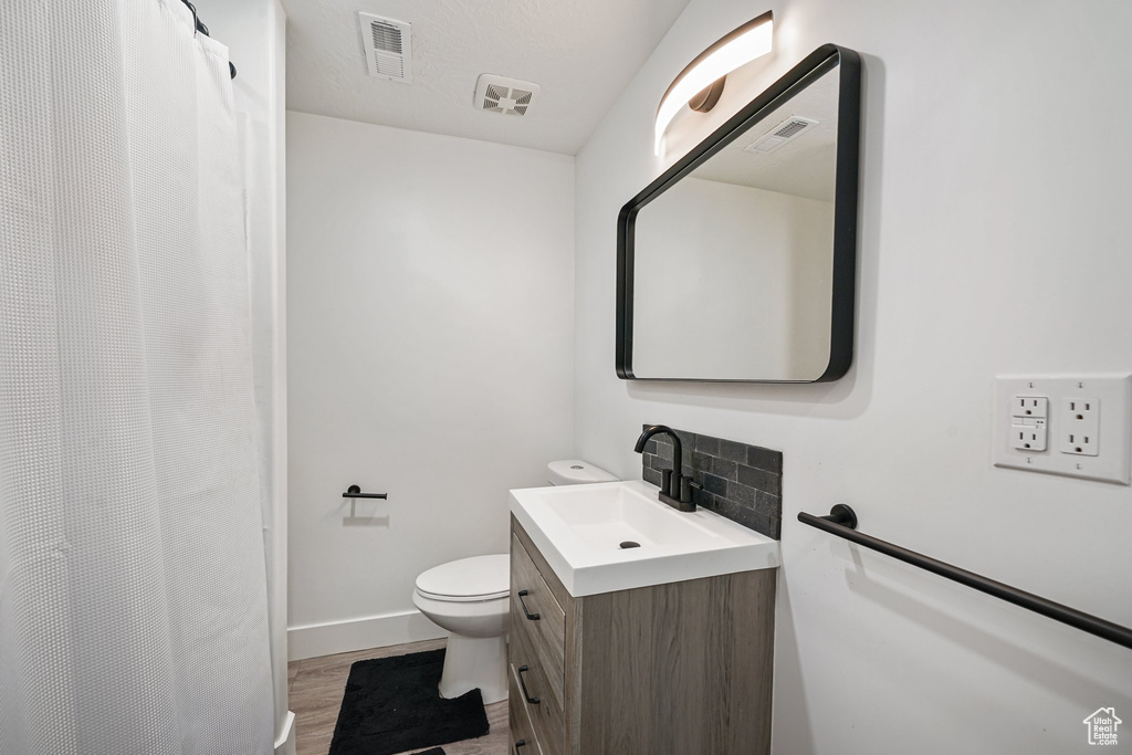 Full bathroom with vanity, toilet, wood finished floors, baseboards, and tasteful backsplash