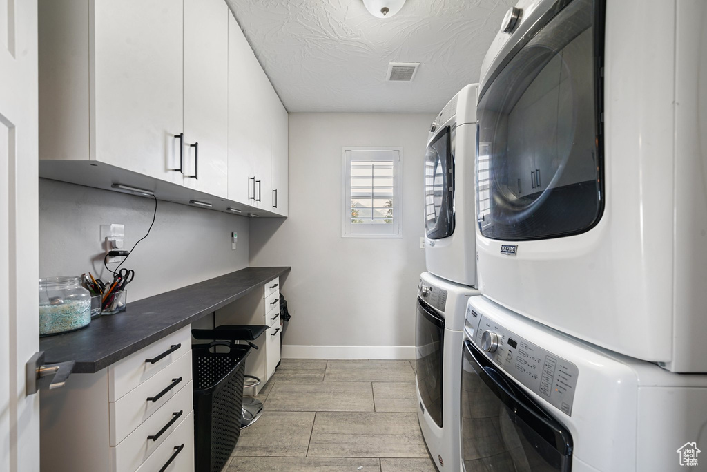 Laundry area with stacked washer / dryer, cabinet space, baseboards, and a textured ceiling