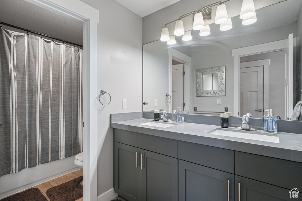 Bathroom with double vanity, toilet, and wood finished floors