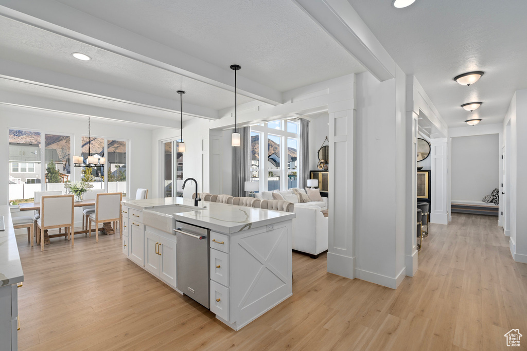 Kitchen with dishwasher, a sink, light stone counters, light wood-style floors, and beamed ceiling