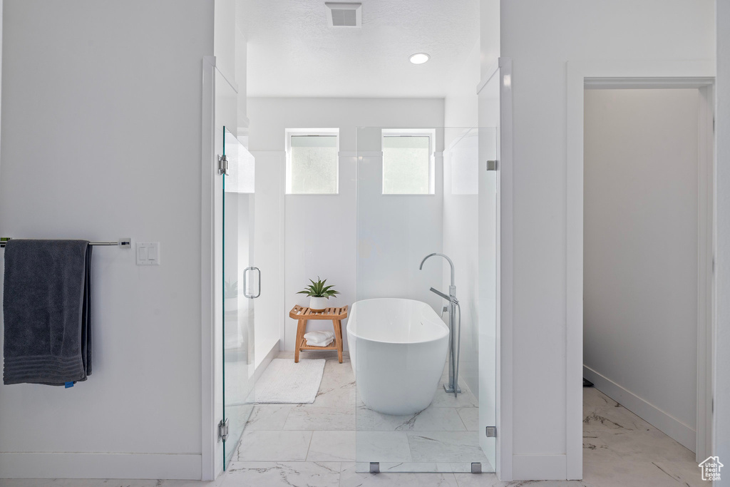 Full bath featuring marble finish flooring, a shower stall, a freestanding tub, and baseboards