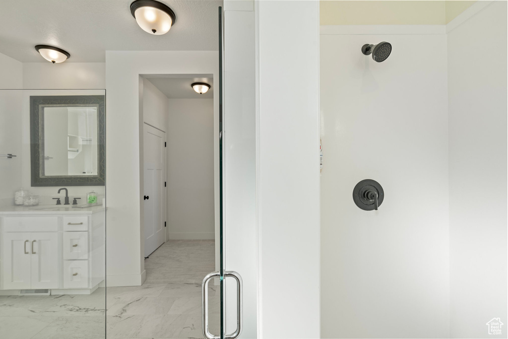 Full bath with marble look tiles, vanity, a shower, and baseboards
