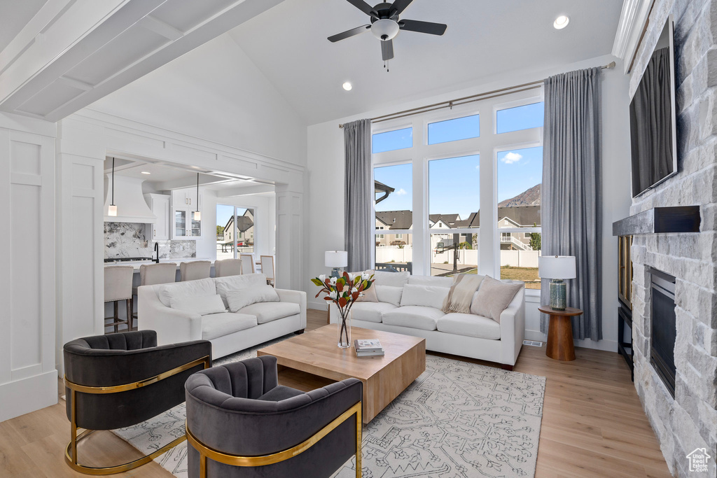 Living area featuring a fireplace, a ceiling fan, light wood-type flooring, and high vaulted ceiling