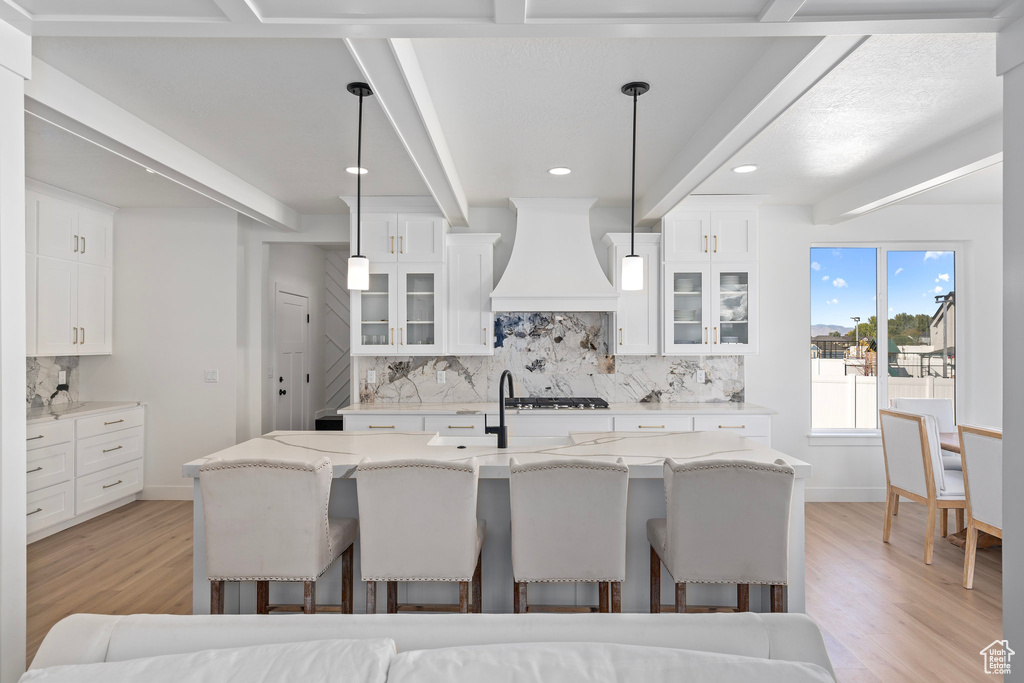 Kitchen with premium range hood, decorative backsplash, light wood-style floors, a kitchen breakfast bar, and beam ceiling