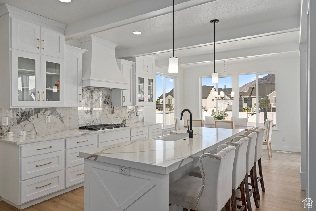 Kitchen featuring a sink, premium range hood, a chandelier, stainless steel gas stovetop, and light wood-style flooring