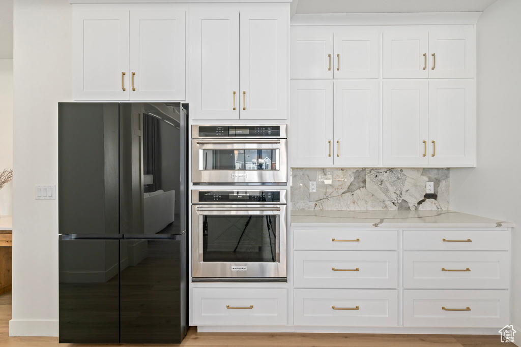 Kitchen with freestanding refrigerator, stainless steel double oven, white cabinetry, and backsplash