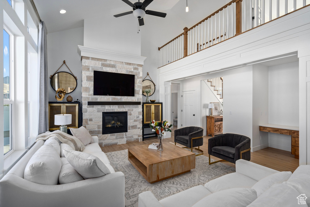 Living room with light wood-style floors, a ceiling fan, healthy amount of natural light, a fireplace, and a high ceiling