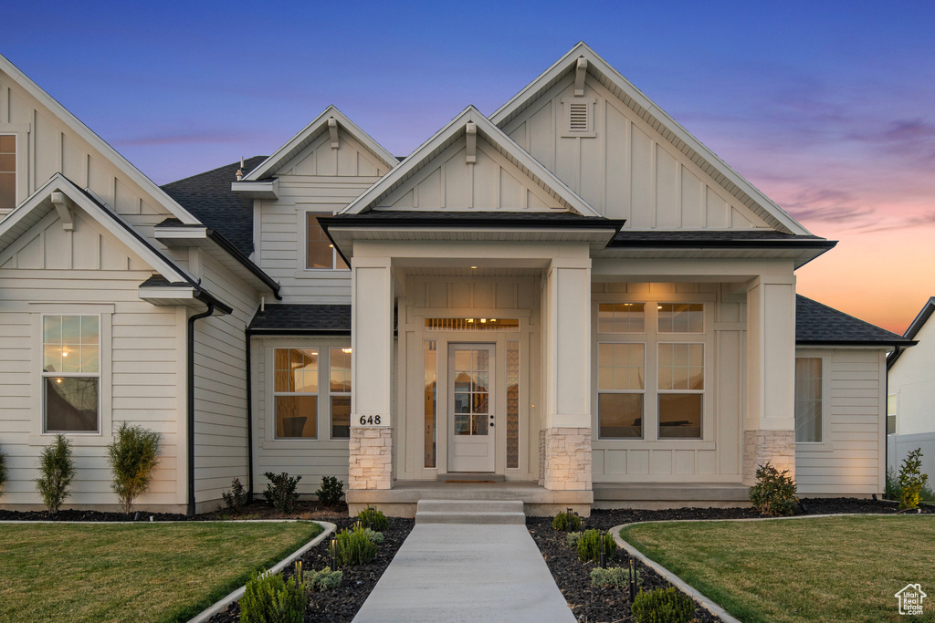 View of front of home featuring board and batten siding, a shingled roof, a front lawn, and stone siding