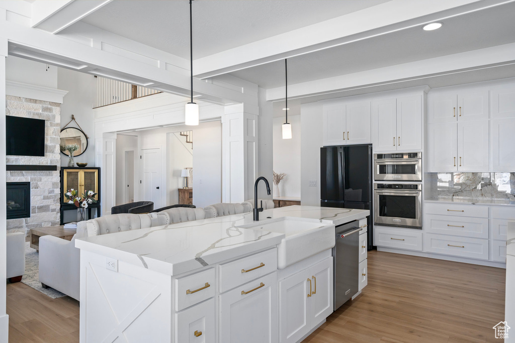 Kitchen with open floor plan, a sink, stainless steel appliances, a stone fireplace, and pendant lighting