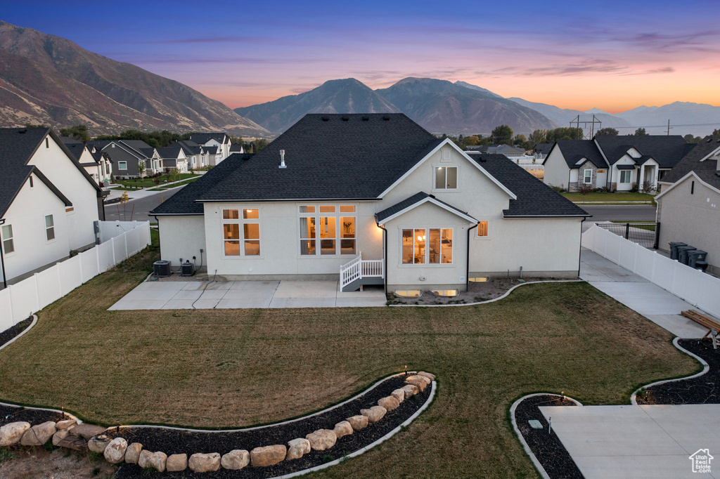 Back of house at dusk with a mountain view, a patio area, roof with shingles, and a residential view
