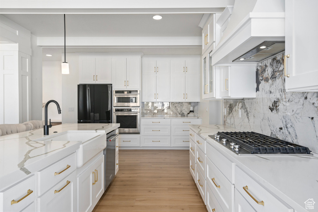 Kitchen featuring appliances with stainless steel finishes, custom exhaust hood, a sink, white cabinets, and recessed lighting