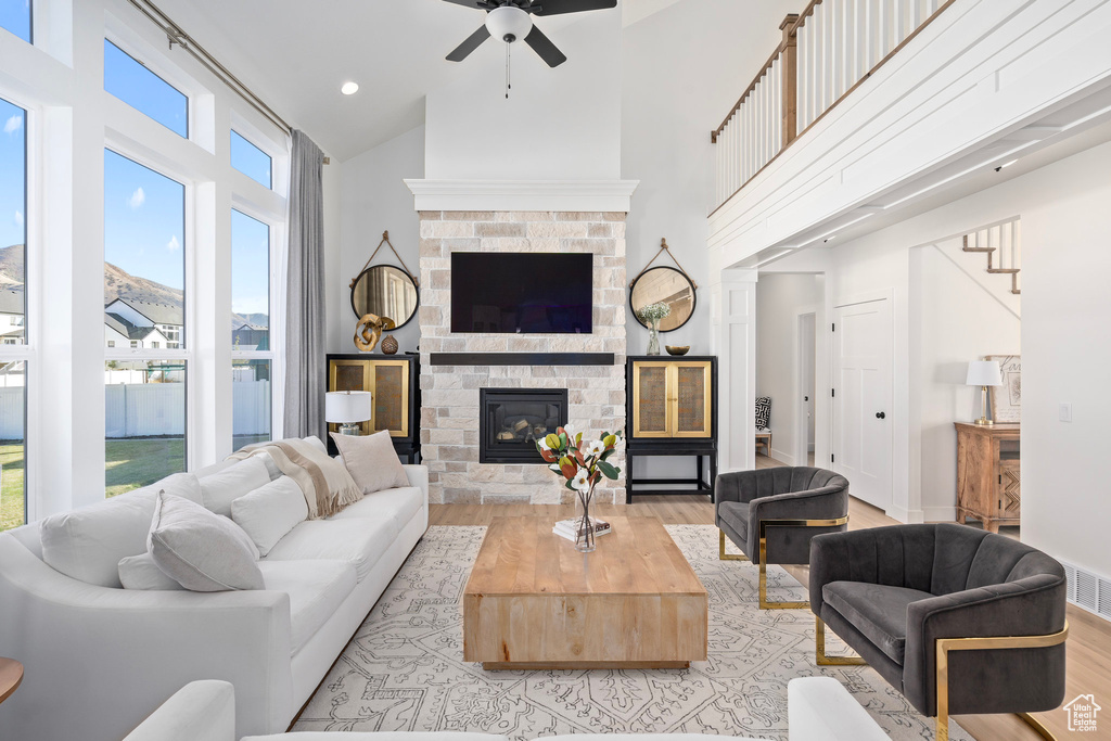 Living room featuring light wood-style floors, high vaulted ceiling, ceiling fan, a glass covered fireplace, and stairway