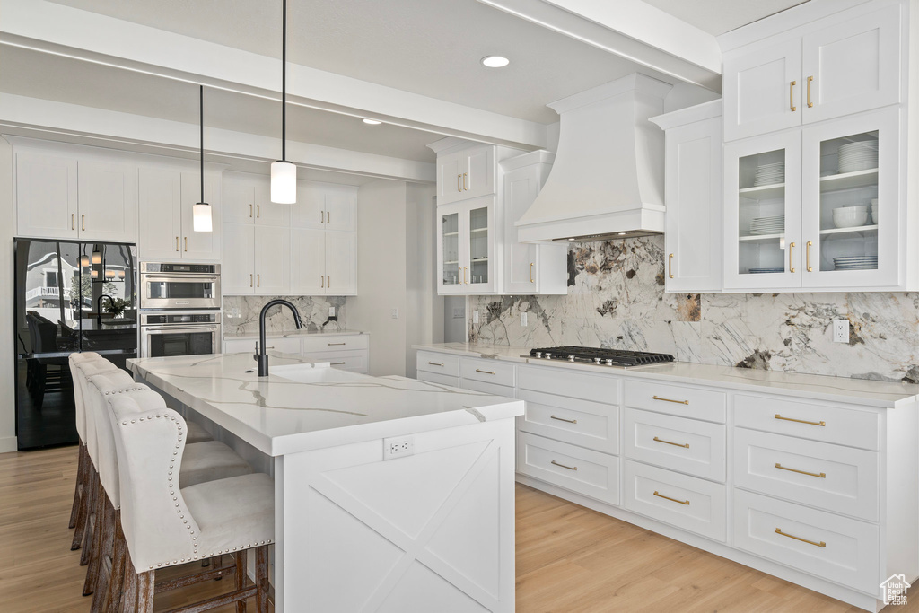 Kitchen with custom exhaust hood, a sink, stainless steel appliances, tasteful backsplash, and white cabinetry