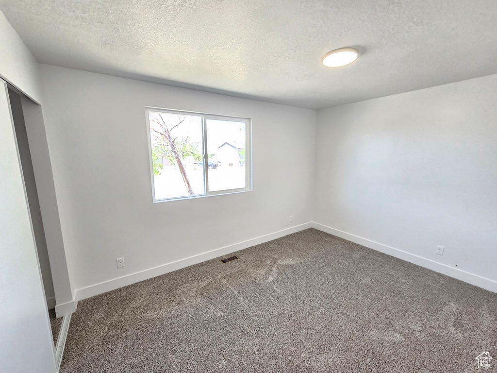 Carpeted empty room with a textured ceiling and baseboards