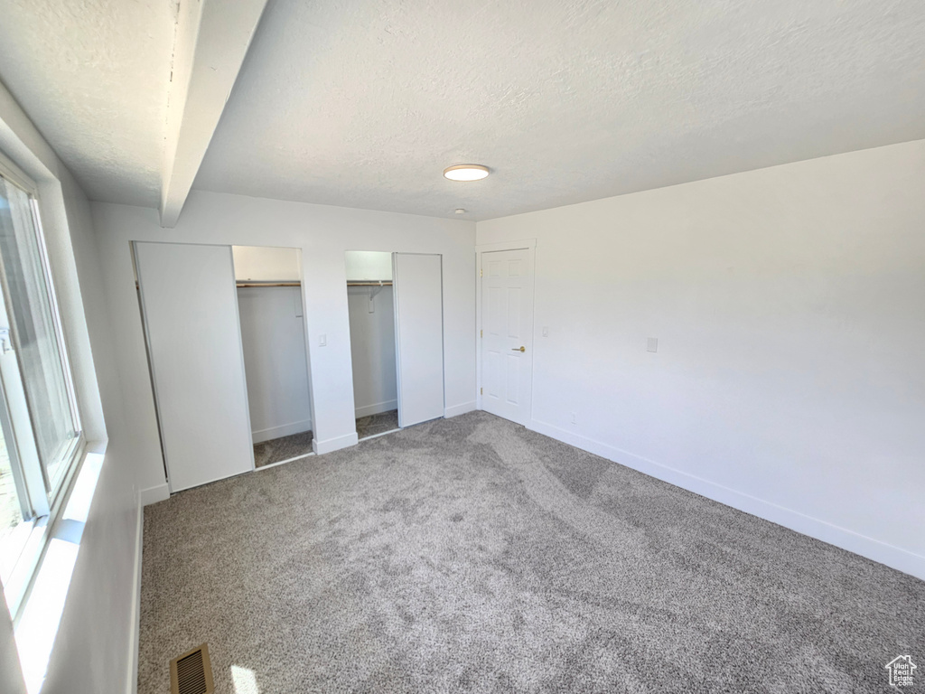 Unfurnished bedroom featuring two closets, a textured ceiling, multiple windows, baseboards, and carpet flooring