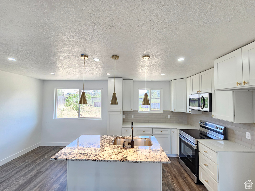 Kitchen featuring appliances with stainless steel finishes, a sink, a textured ceiling, decorative backsplash, and dark wood-type flooring