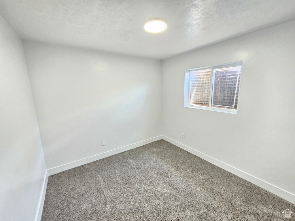 Spare room featuring dark carpet, baseboards, and a textured ceiling