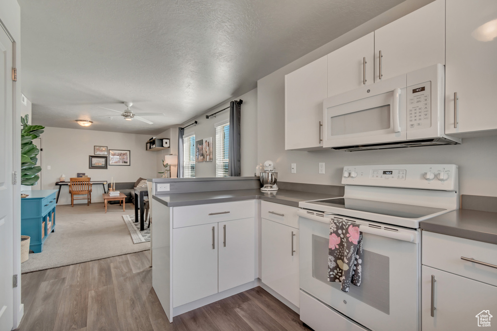 Kitchen featuring white appliances, ceiling fan, wood finished floors, a peninsula, and a textured ceiling