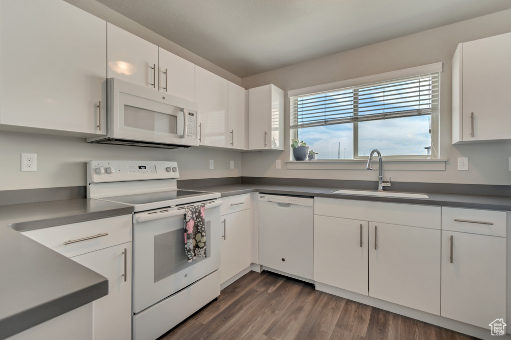 Kitchen with white appliances, a sink, plenty of natural light, and dark countertops