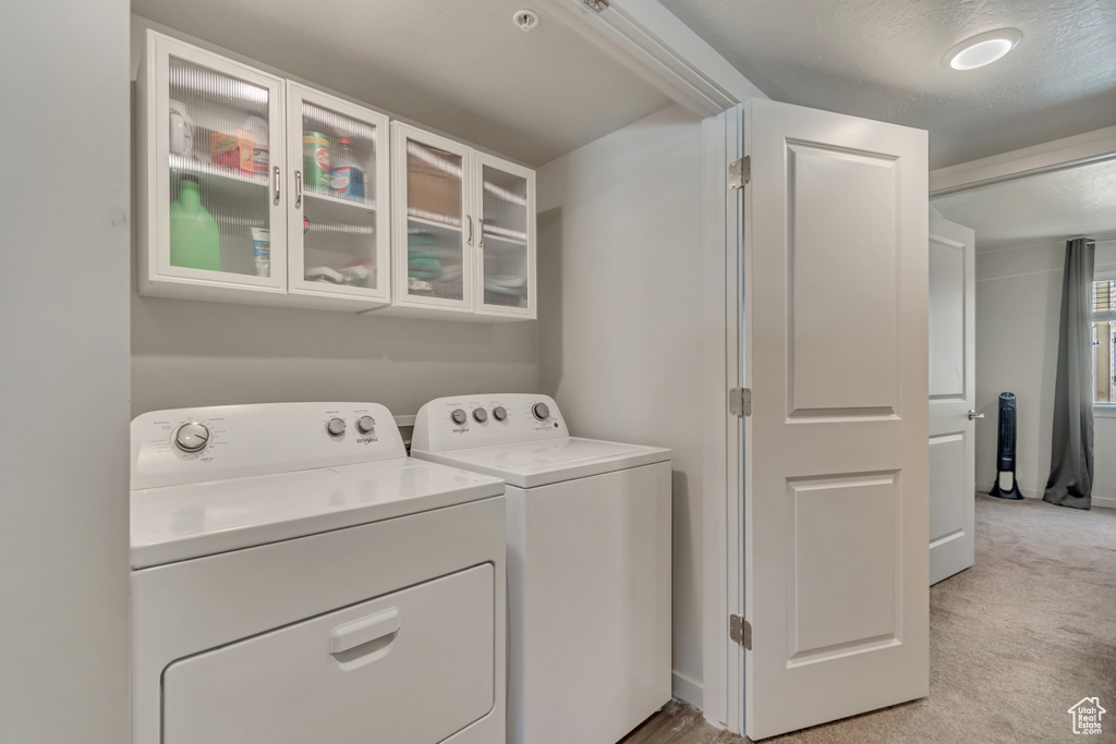 Laundry area with separate washer and dryer, light carpet, and baseboards
