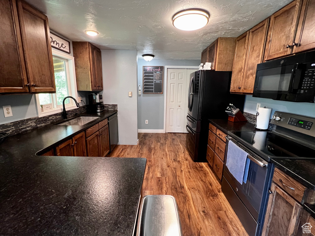 Kitchen featuring black appliances, a sink, wood finished floors, and baseboards