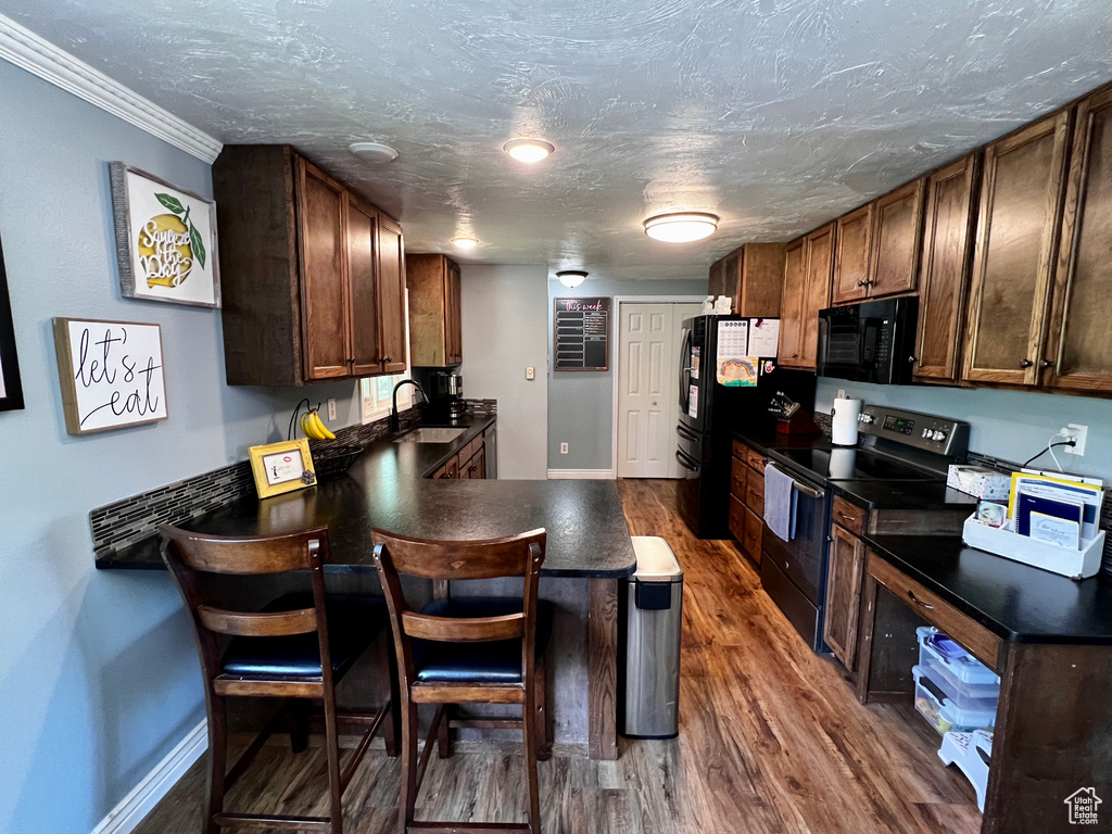 Kitchen with black appliances, a sink, dark countertops, a peninsula, and ornamental molding