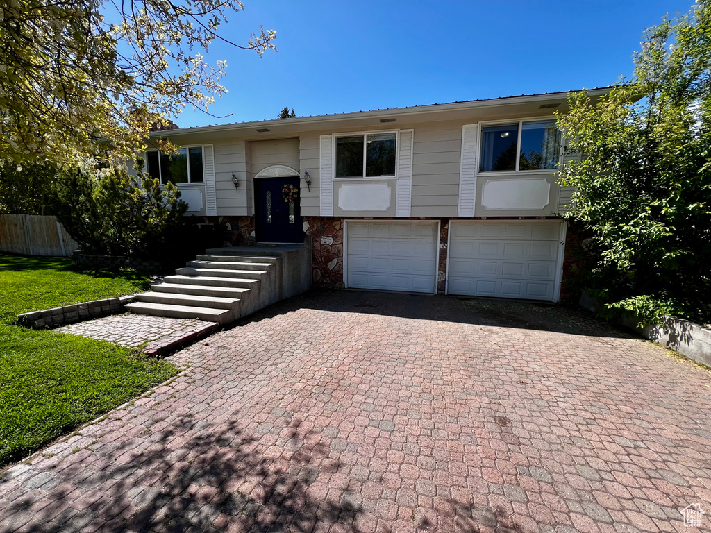 Raised ranch featuring an attached garage, decorative driveway, and stone siding