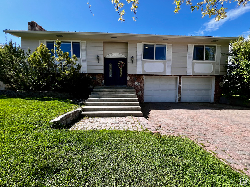 Raised ranch with a garage, a front yard, decorative driveway, and a chimney