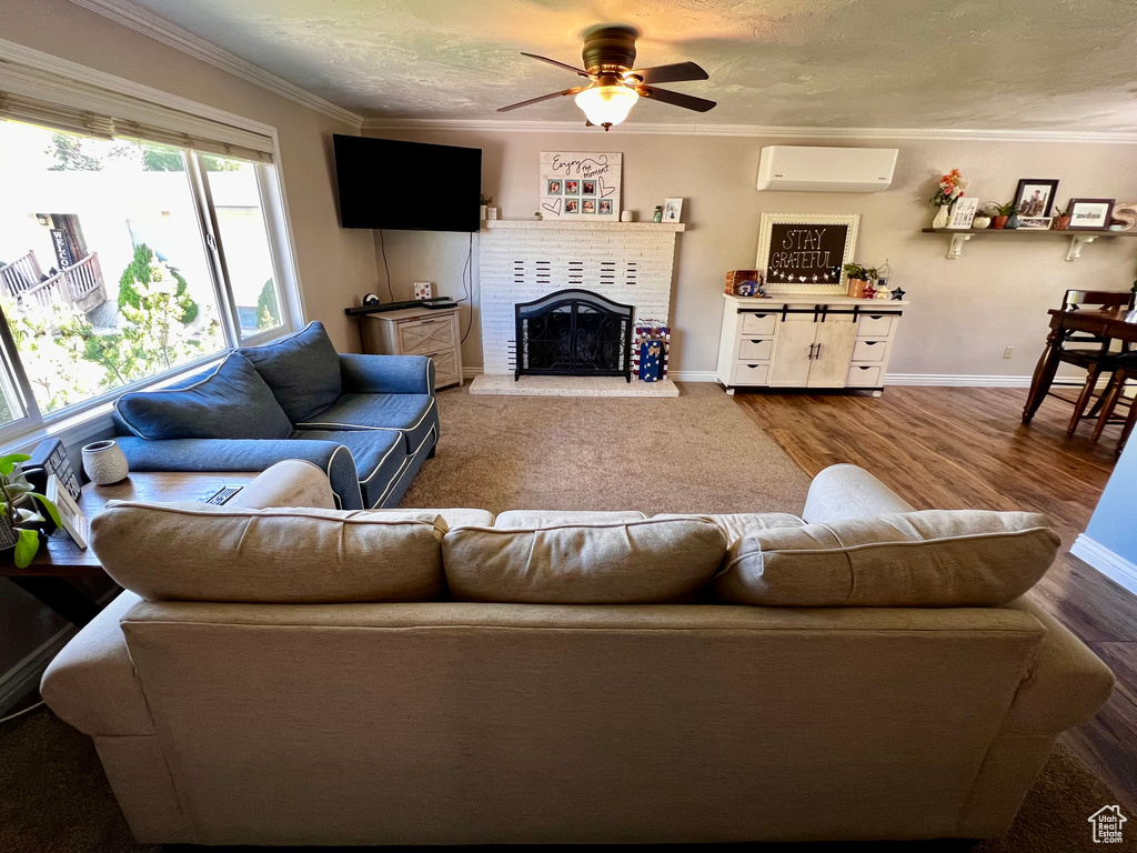 Living room featuring an AC wall unit, a ceiling fan, a brick fireplace, ornamental molding, and baseboards