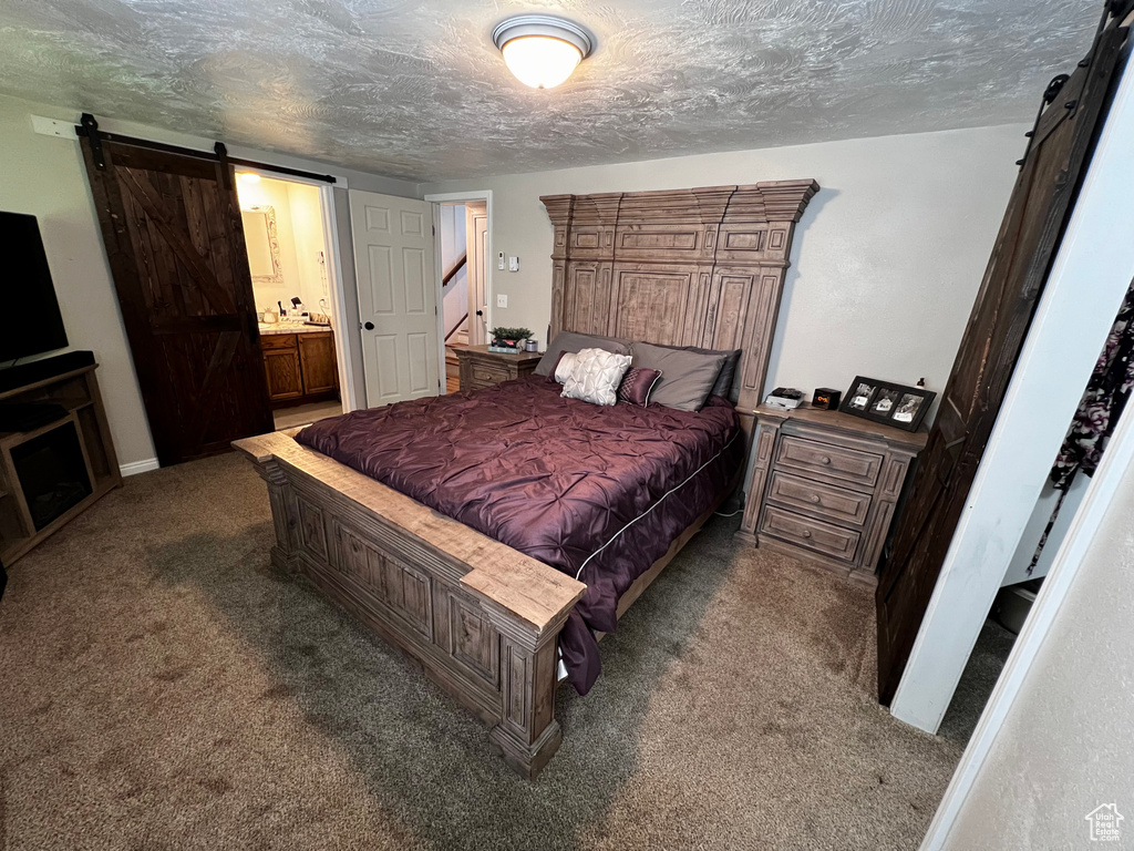 Carpeted bedroom with a barn door, a textured ceiling, and ensuite bath