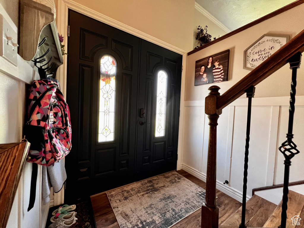 Foyer with a decorative wall, wood finished floors, a wainscoted wall, and ornamental molding