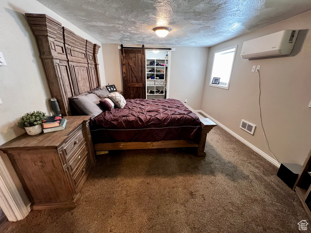 Bedroom with an AC wall unit, a barn door, dark colored carpet, a textured ceiling, and baseboards