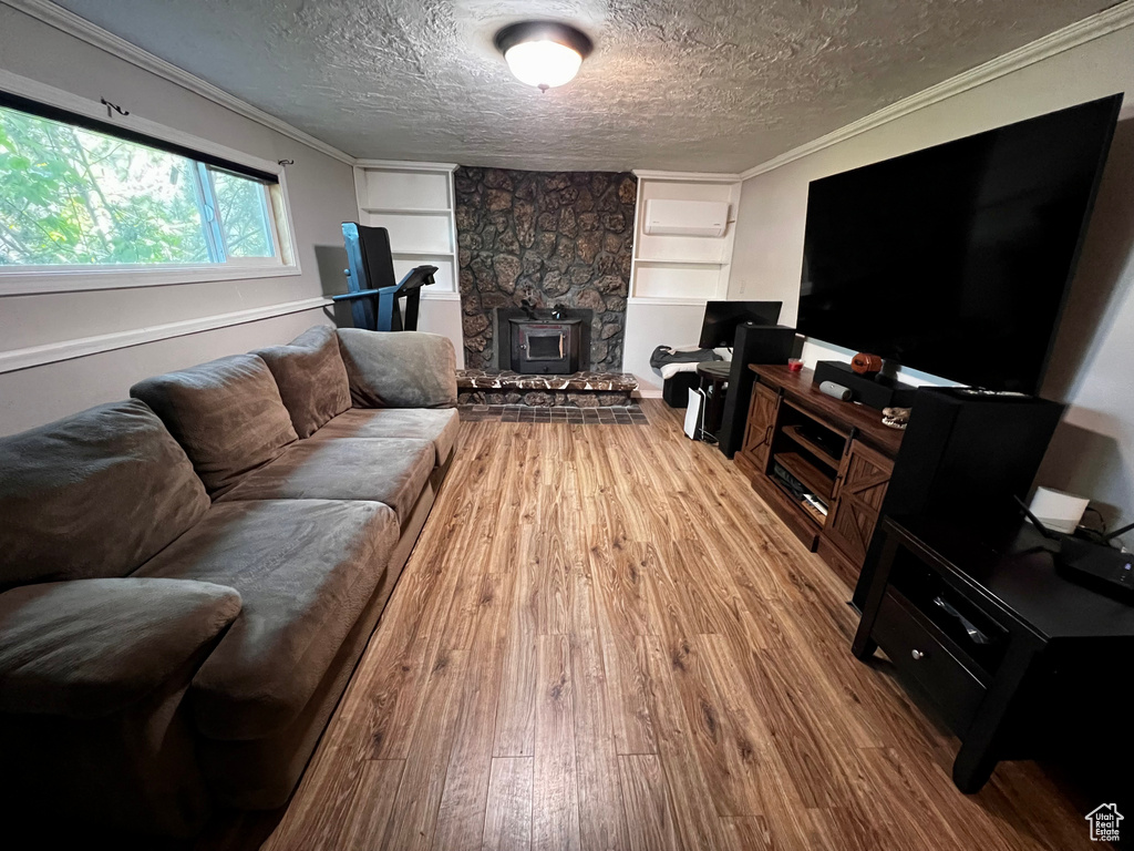 Living area with wood finished floors, built in shelves, a textured ceiling, crown molding, and a wood stove