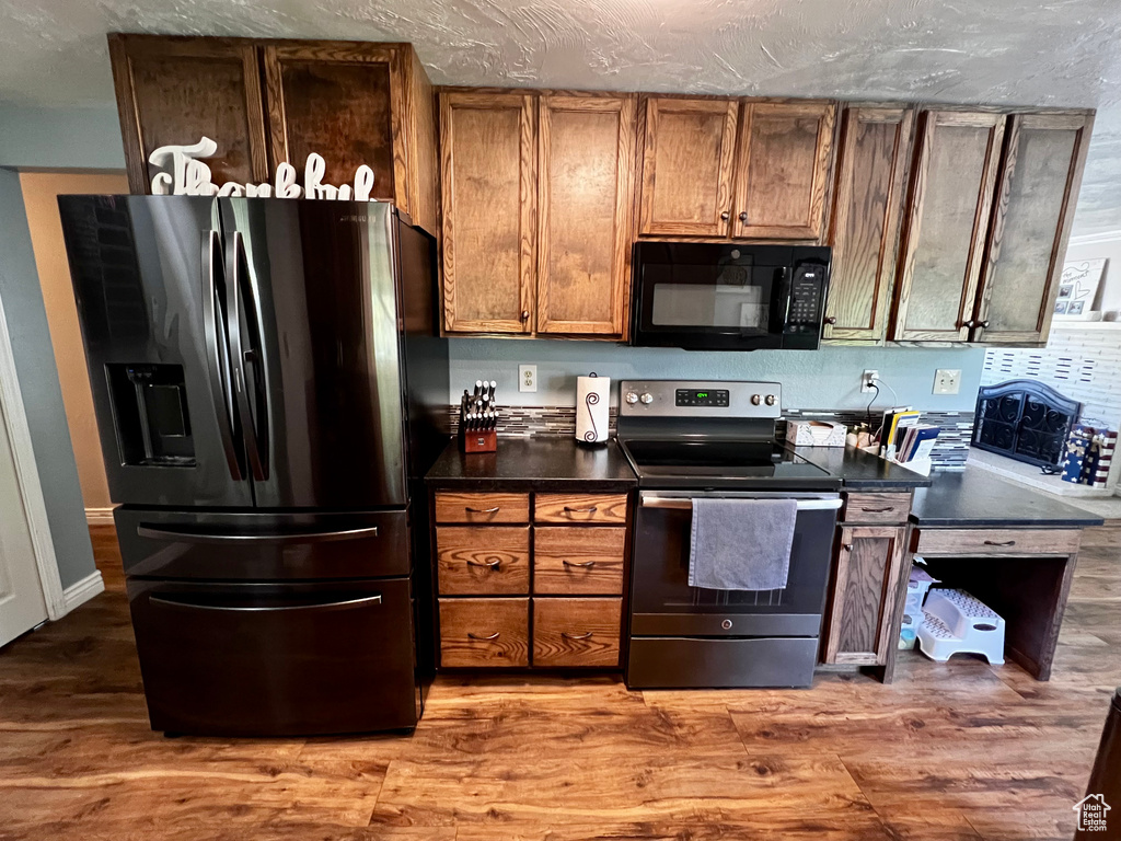 Kitchen featuring black appliances, dark countertops, brown cabinets, and wood finished floors