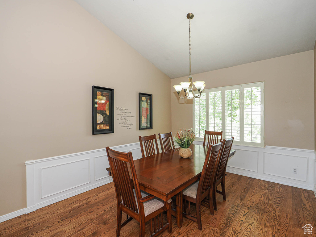 Dining space with wood finished floors, a chandelier, vaulted ceiling, a decorative wall, and wainscoting