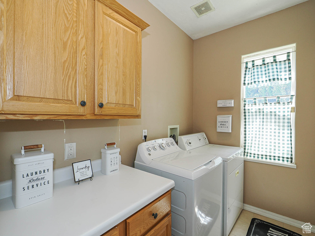 Washroom with cabinet space, washing machine and dryer, baseboards, and light tile patterned flooring