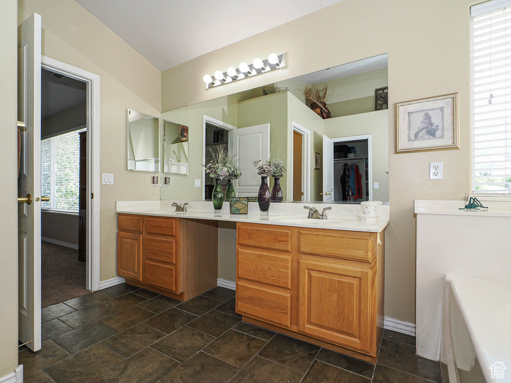 Bathroom featuring plenty of natural light, double vanity, baseboards, and a walk in closet