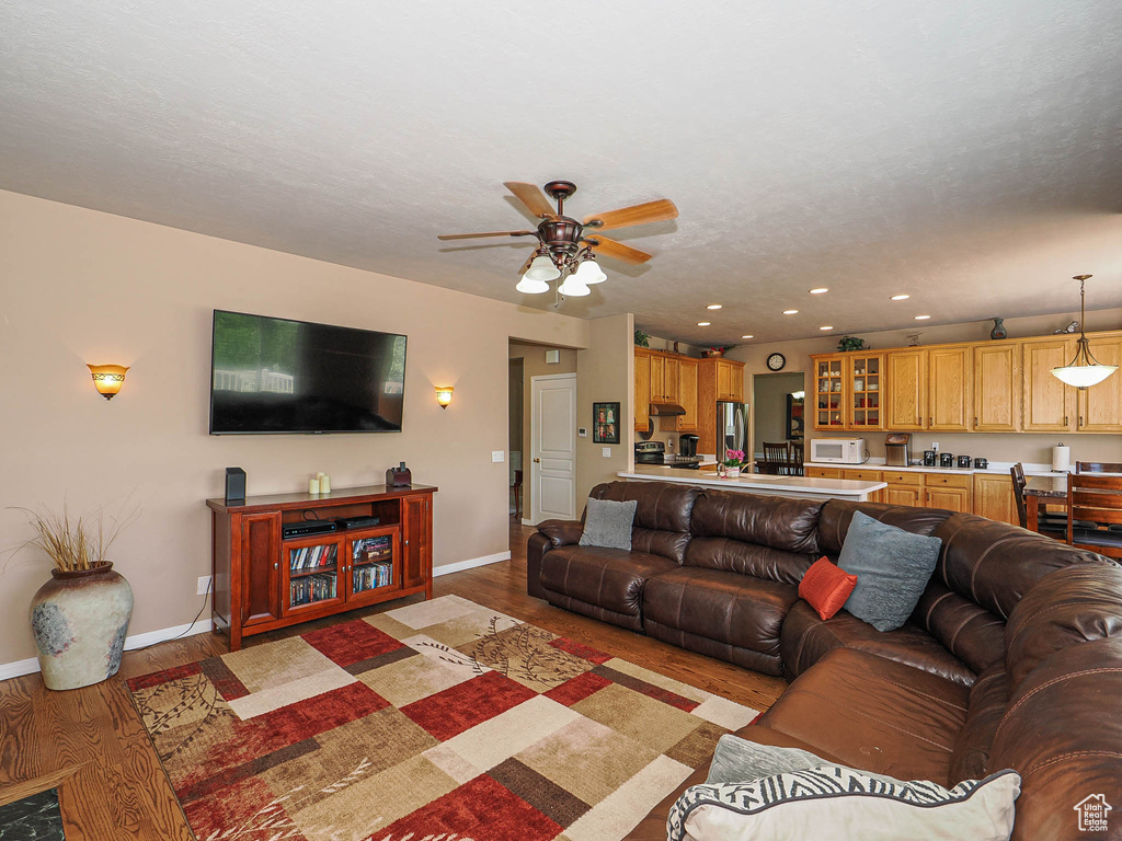 Living area featuring light wood-type flooring, a ceiling fan, baseboards, and recessed lighting