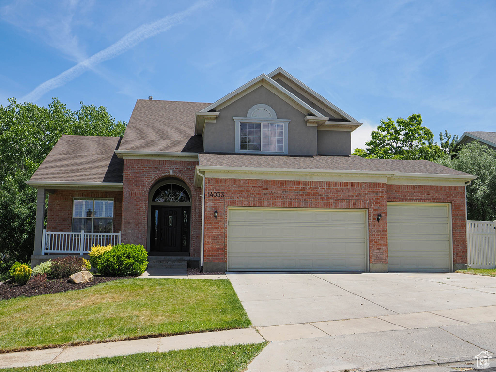 Traditional home featuring concrete driveway, a front lawn, a shingled roof, brick siding, and covered porch