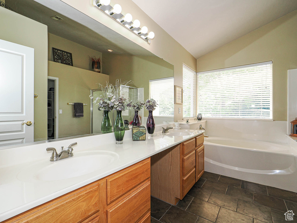 Full bathroom featuring double vanity, a garden tub, vaulted ceiling, and stone finish floors