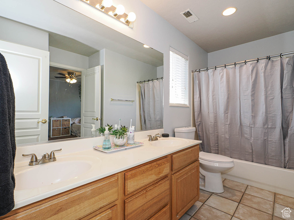 Ensuite bathroom featuring toilet, double vanity, tile patterned floors, a ceiling fan, and shower / bath combo