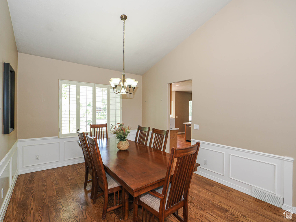 Dining area with lofted ceiling, wood finished floors, a decorative wall, a chandelier, and a wainscoted wall