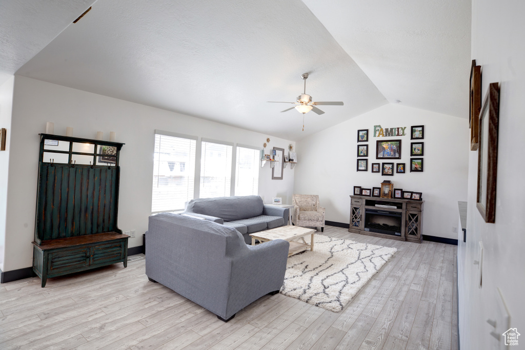 Living area with a ceiling fan, vaulted ceiling, light wood finished floors, and baseboards