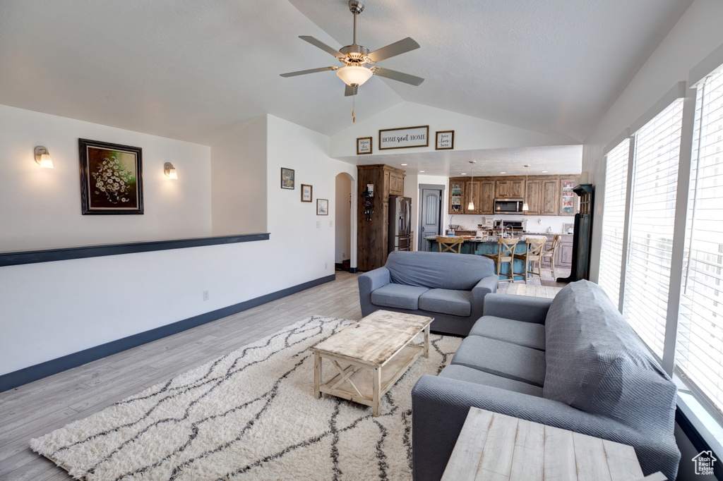 Living room featuring arched walkways, ceiling fan, light wood-style flooring, baseboards, and high vaulted ceiling