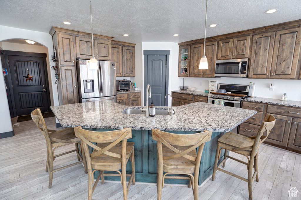 Kitchen featuring appliances with stainless steel finishes, a sink, arched walkways, a breakfast bar, and a center island with sink