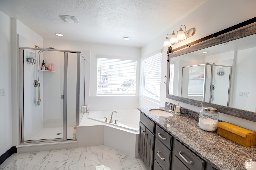 Full bathroom featuring vanity, a shower stall, a bath, marble look tiles, and a textured ceiling