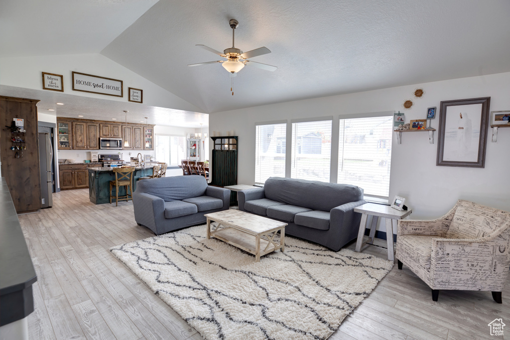 Living room with ceiling fan, light wood-style flooring, and high vaulted ceiling