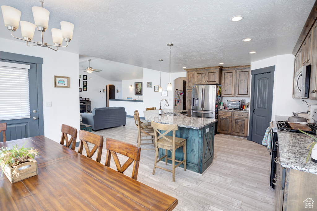 Dining area with a textured ceiling, a ceiling fan, light wood finished floors, a chandelier, and recessed lighting