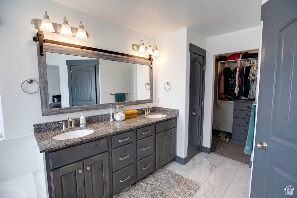 Full bathroom with double vanity, marble look tiles, a walk in closet, and a tub to relax in