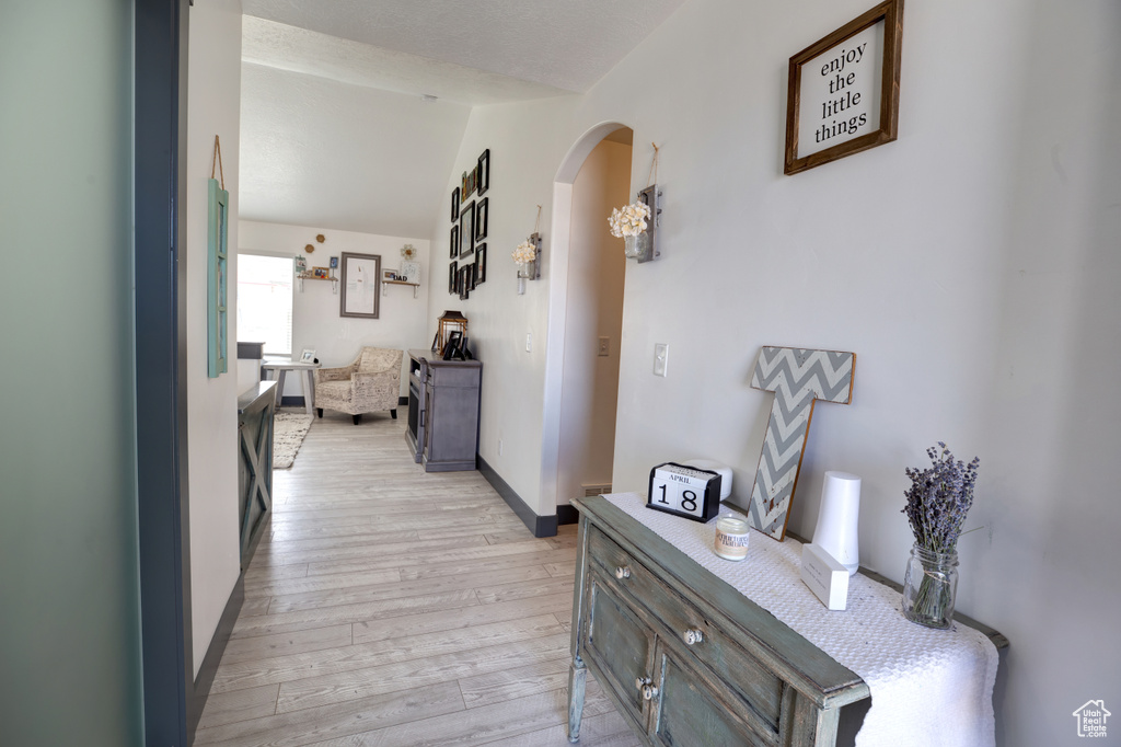 Corridor featuring arched walkways, light wood-style flooring, lofted ceiling, and baseboards